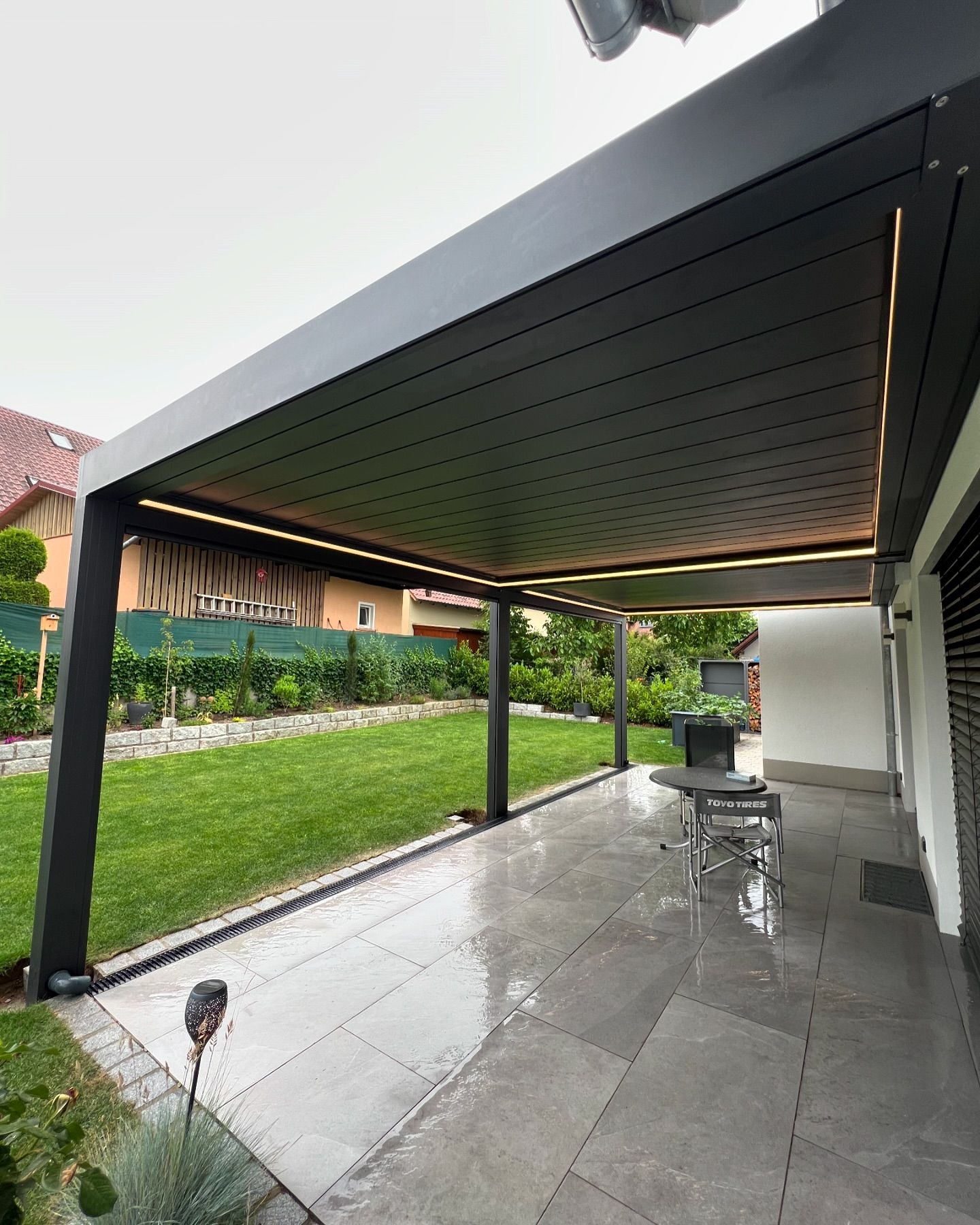 Realizovaná černá pergola kotvená k domu s integrovaným LED osvětlením
